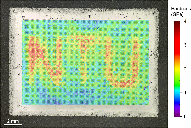 Meso-scale Hardness map of a sample with site-specific properties, which is superimposed to the optical micrograph of the polished sample surface. The schematic at the bottom right corner illustrates the 3D design of the sample.